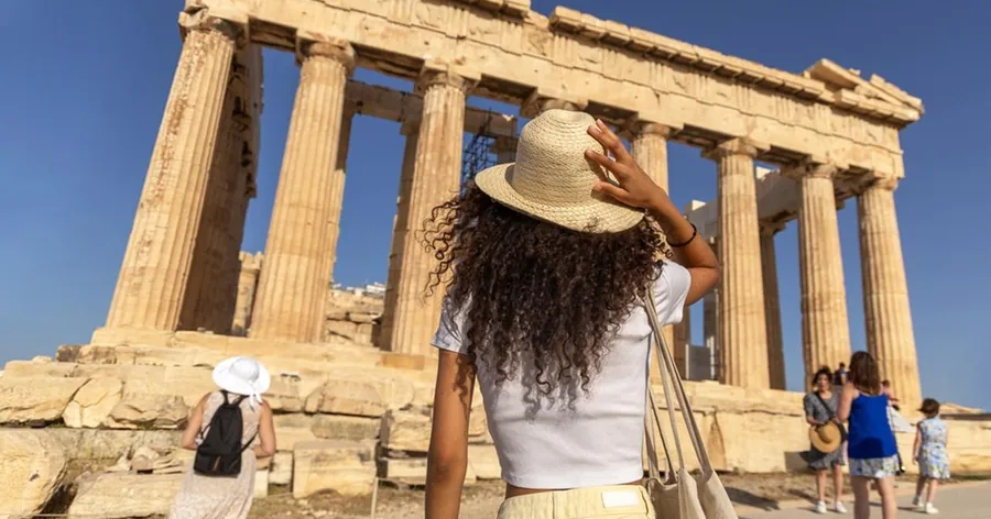 Επισκέπτρια με ψάθινο καπέλο κοιτάζει ψηλά τους κίονες του Παρθενώνα